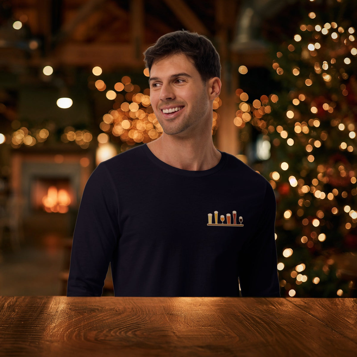 Smiling man in the navy Christmas Flight 2026 long sleeve tee at a holiday taproom with a lit Christmas tree