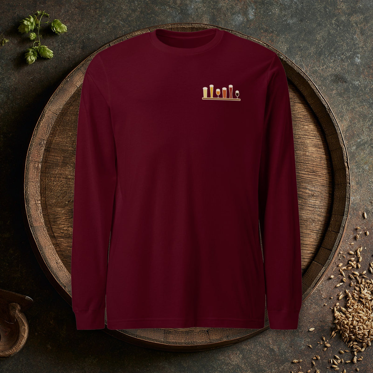 Christmas Flight 2026 Long Sleeve T-Shirt in Maroon laid flat on an oak barrel top with hops and malt
